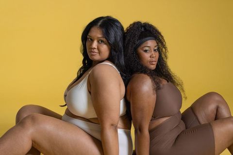 Curvy diverse duo modeling lingerie and athleisure back-to-back on warm yellow backdrop