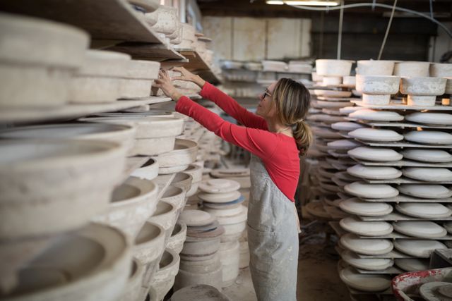 Female potter placing craft product in shelf in pottery workshop