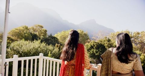 Indian women wearing sarees standing on white balcony gazing over misty mountain valley