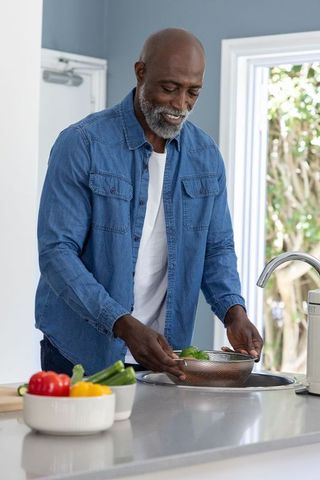 African american senior man rinsing greens at kitchen sink preparing fresh vegetables