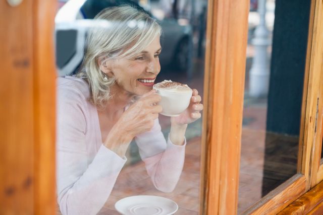 Smiling senior woman drinking coffee while sitting by table at cafe shop