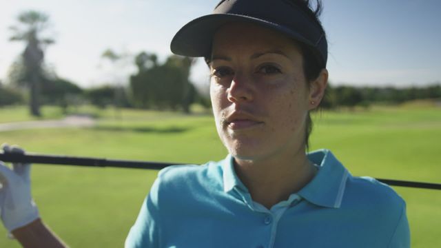 Woman golfer wearing visor and glove stands confidently with golf club on shoulders. Sunlit green course stretches in background, suggesting a carefree, active lifestyle. Useful for promoting sports events, portraying women in sports, or illustrating empowerment and confidence in advertising or editorial contexts.