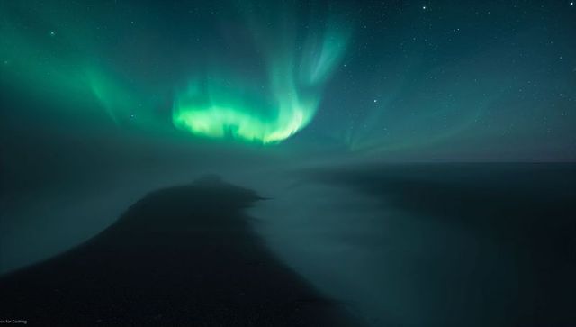 Aurora borealis dancing over misty arctic peninsula night sky starry seaside ethereal green light