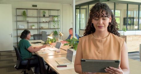 Young professional using tablet in modern coworking office with team collaborating over laptops