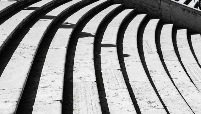 Curving travertine steps casting bold shadows in high-contrast monochrome