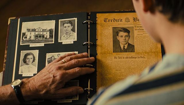 Senior guiding grandson through family scrapbook with vintage portraits and aged newspaper