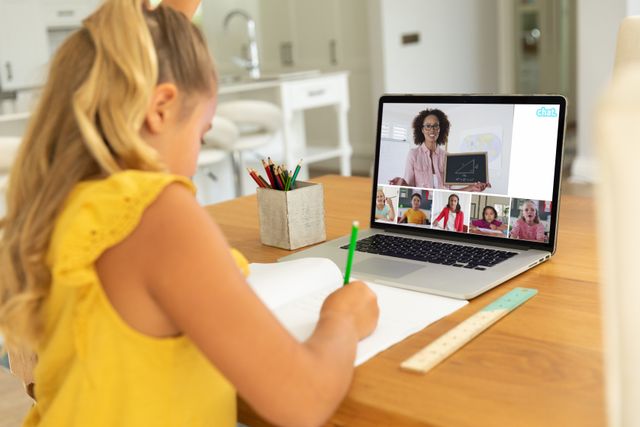 Caucasian girl writing in book while studying online through video call on laptop at home. Screen, internet, unaltered, childhood, wireless technology, education, student and e-learning concept.