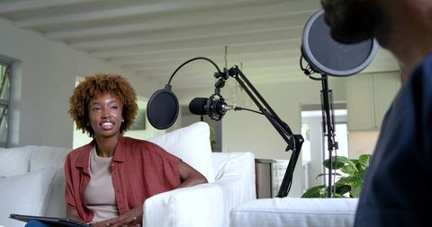 African american co-hosts recording podcast in bright living room home studio with microphones