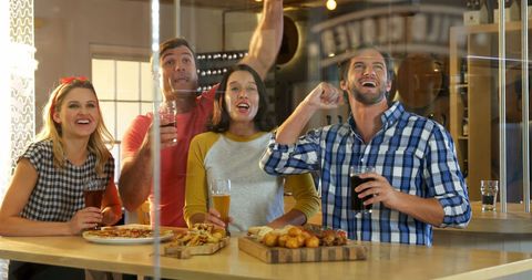 Excited friends enjoying pizza and drinks while watching game