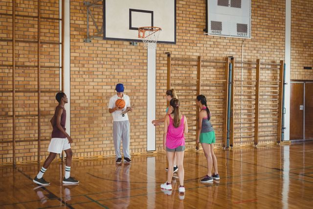 High school basketball team practicing under the guidance of a coach in a gym. Ideal for use in educational materials, sports training guides, youth fitness programs, and promotional content for school athletic events.