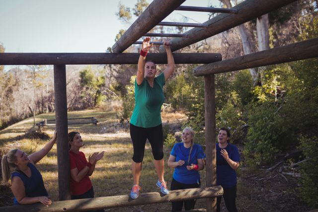 Woman being cheered bye her teammates to climb monkey bars during obstacle course training in the boot camp
