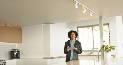 African american man holding tablet at modern sunlit kitchen island, looking up