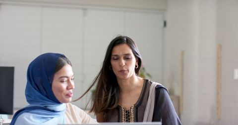 Indian female colleagues collaborating over laptop at modern coworking workspace