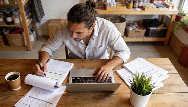 Young entrepreneur managing bookkeeping and laptop on rustic wooden cafe table for small business