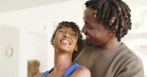 Sunlit african american couple laughing and embracing in minimalist home interior