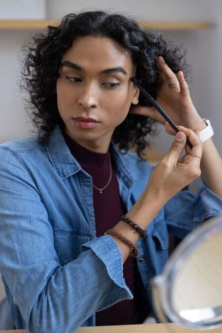 Non-binary person applying eyeshadow at vanity holding hair back closeup beauty routine