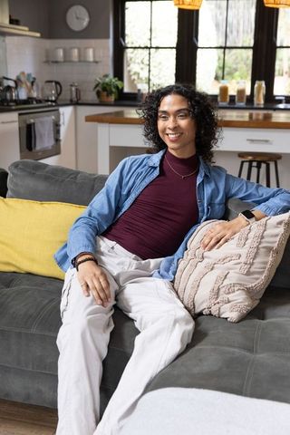 Non-binary person relaxing on sofa in cozy open-plan living room denim shirt and smartwatch