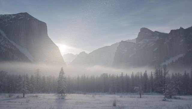 Dawn light shining through mist over snow-covered valley and granite cliffs