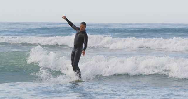 Male surfer in black wetsuit balancing on surfboard while riding wave on sunny day. Ideal for content related to water sports, surfing techniques, coastal lifestyle, outdoor activities, and beach vacations.