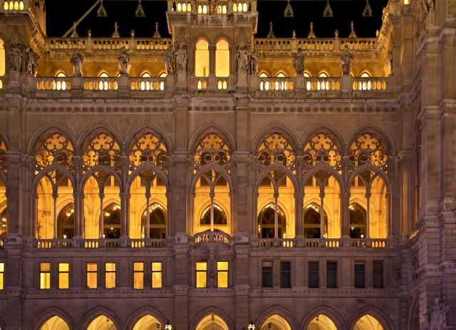 Close-up of Gothic building facade illuminated at night, featuring detailed arches and windows. Ideal for use in articles on European architecture, tourism promotions, historic buildings, and educational materials about Gothic design.