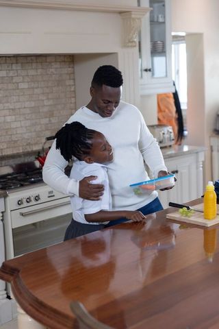 African american father hugging daughter on kitchen island while packing lunch with grapes