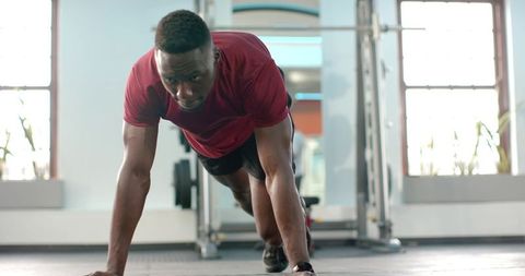 African american man performing intense plank core workout in modern gym natural light