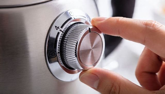 Turning metallic rotary knob on stainless steel appliance close-up, numeric dial detail