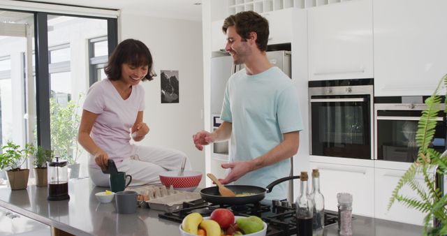 Young couple cooking breakfast and enjoying time together in modern kitchen. Perfect for content related to relationships, cooking at home, modern appliances, and domestic life.