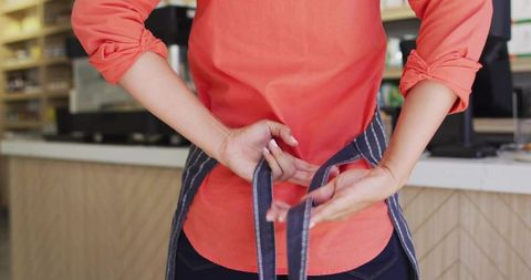 Cafe Staff Tying Apron Behind Counter in Coffee Shop