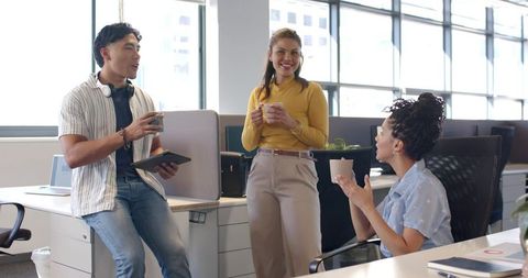 Casual office team enjoying coffee break and brainstorming while holding tablets and mugs