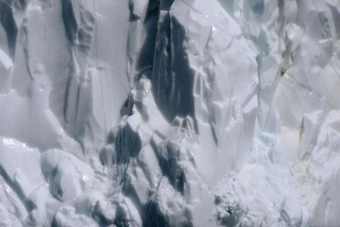 Abstract glacial ice wall with deep crevasses, sculpted ice textures and blue shadows