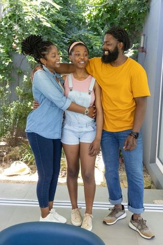 African american parents hugging smiling teen daughter on sunlit garden patio