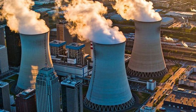 Cooling towers releasing steam over urban power plant and rail yard at golden hour