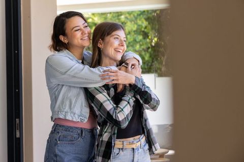 Diverse female couple embracing on home patio smiling in casual denim and plaid