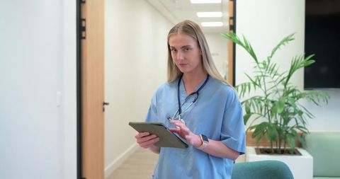 Young nurse using tablet in modern clinic corridor with stethoscope and minimalist lounge