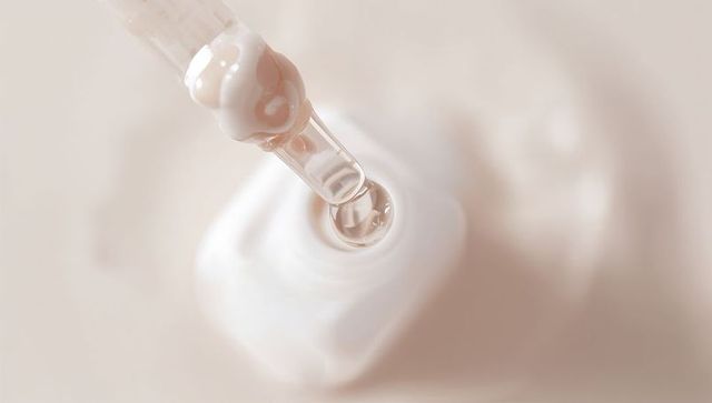 Clear pipette dripping beige serum onto creamy swirl cosmetic skincare dropper close-up