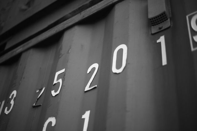 Monochrome close-up of a shipping container featuring the number '5201' prominently. Ideal for use in industrial or logistics themed projects, articles related to freight transport and shipping, or minimalist design concepts focusing on forms and structure.