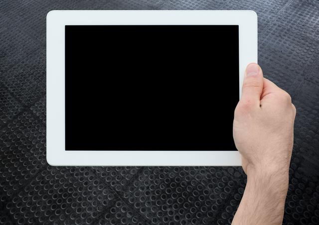 Hand holding tablet with blank screen, suitable for technology, advertising, app presentations, or digital content mockups. Dark textured floor generates contrast, highlighting the device.