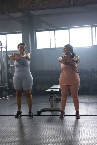 African american women stretching arms and smiling in gym during partner workout session