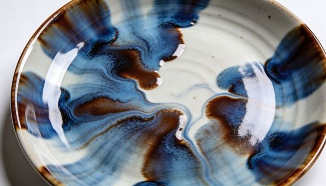 Handmade wheel-thrown ceramic bowl with flowing blue and brown glaze, glossy artisan vessel