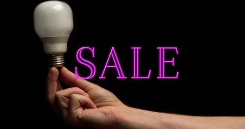 Hand holding led bulb beside neon sale sign on black background energy saving promotion