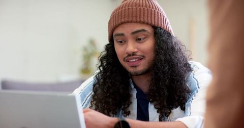Mid-adult man working on laptop wearing beanie and smartwatch in cozy coworking space
