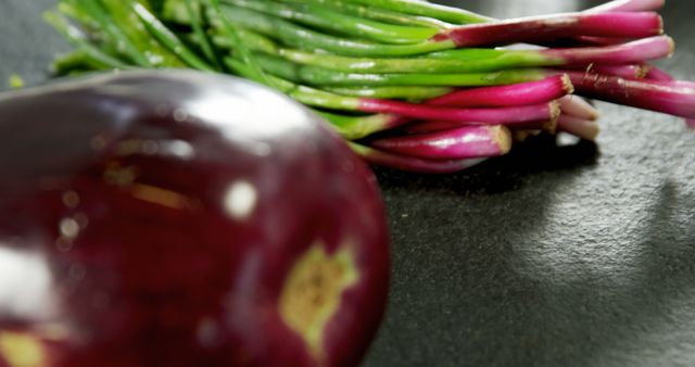 Close-up showing a fresh sliced eggplant and a bunch of spring onions ready for culinary use. Perfect for use in content related to cooking, healthy eating, vegetable preparation, and kitchen activities.