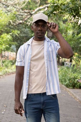 African american man adjusting cap on park pathway wearing striped shirt and jeans
