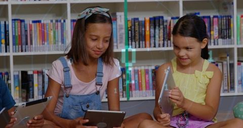 Two Girls Sitting in Library Using Tablets Sharing Digital Learning and Friendship
