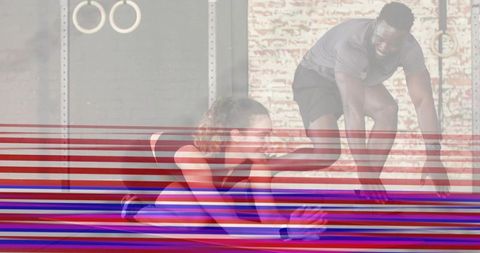 Trainer assisting client with seated forward stretch on mat in urban gym with rings