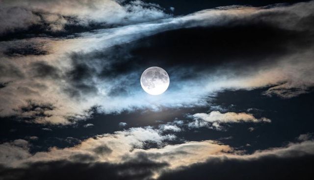 Full Moon Shining Through Layered Clouds with Soft Halo and Dramatic Night Sky