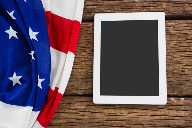 This image shows an American flag draped next to a digital tablet on a wooden table. It can be used for themes related to patriotism, national holidays, technology in America, or modern communication. Ideal for websites, blogs, or advertisements focusing on American culture, technology, or national events.