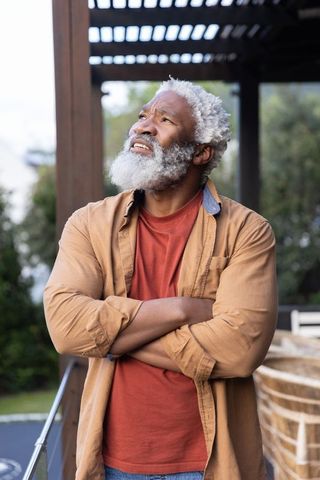 Contemplative senior african american man standing on sunlit backyard deck under pergola