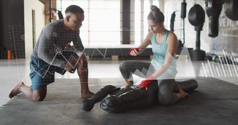 Coach observing trainee wrapping hands and handling heavy bag in boxing training